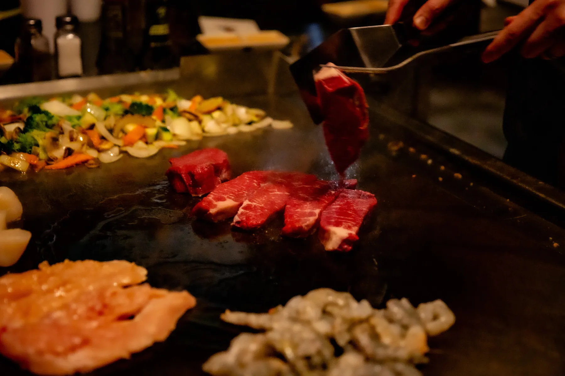 Steak, chicken, and vegetables cooking on a hibachi grill