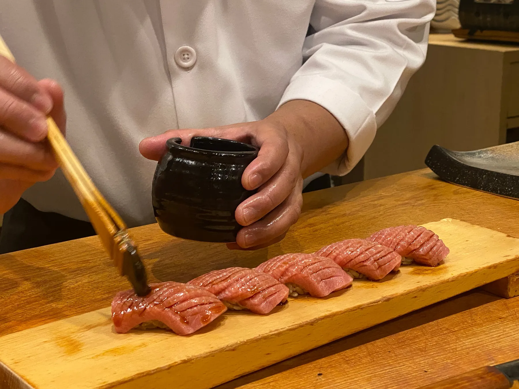 Sushi chef brushing a row of seared nigiri